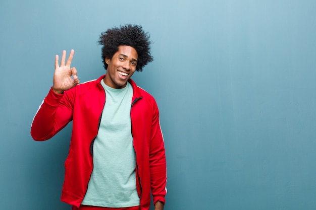 Joven deportista negro sentirse feliz, relajado y satisfecho, mostrando aprobación con gesto bien, sonriendo en la pared del grunge