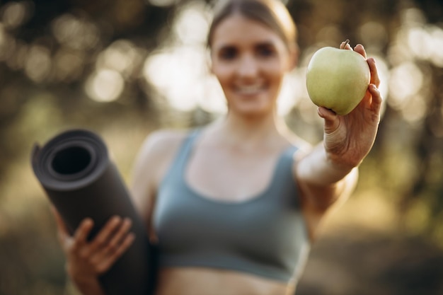 Joven deportista en el parque sosteniendo estera y manzana