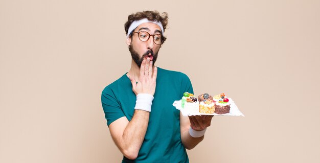 Joven deportista con pasteles contra la pared plana