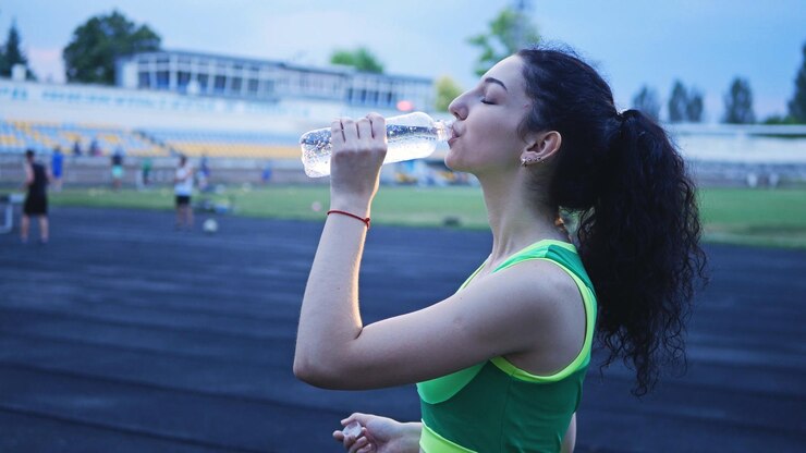 Una joven deportista con el pelo rizado bebe agua después de correr La deportista en el estadio