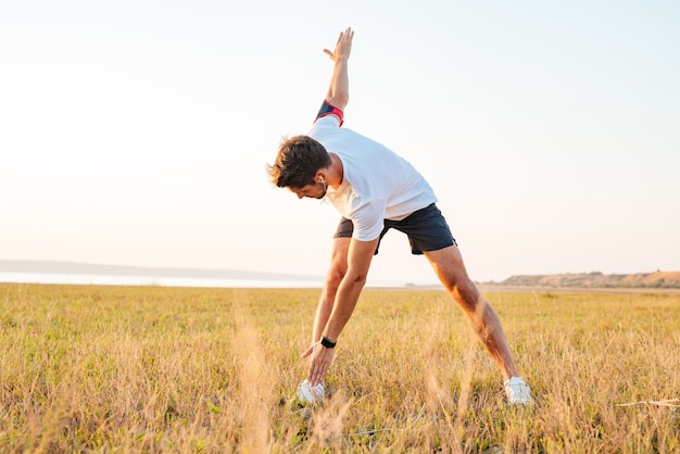 Joven deportista de pie y estirando al aire libre por la mañana