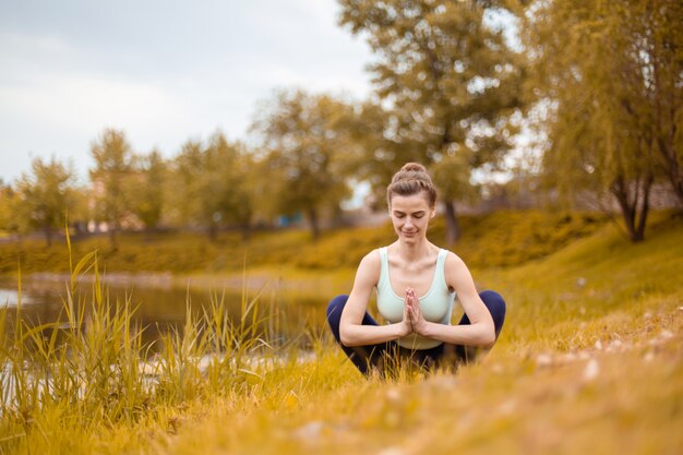 Una joven deportista practica yoga en un césped de otoño amarillo junto al río, usa la postura de asaltos de yoga. meditación y unidad con la naturaleza.