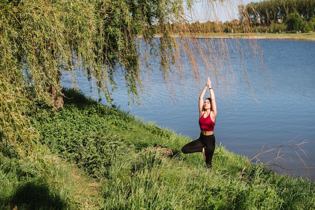 Joven deportista practicando yoga al aire libre a orillas del lago