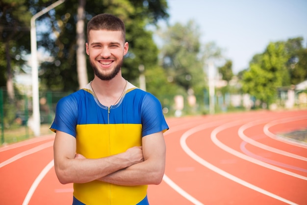 Joven deportista profesional felizmente mirando a la cámara mientras pasa tiempo en la cinta de correr del estadio