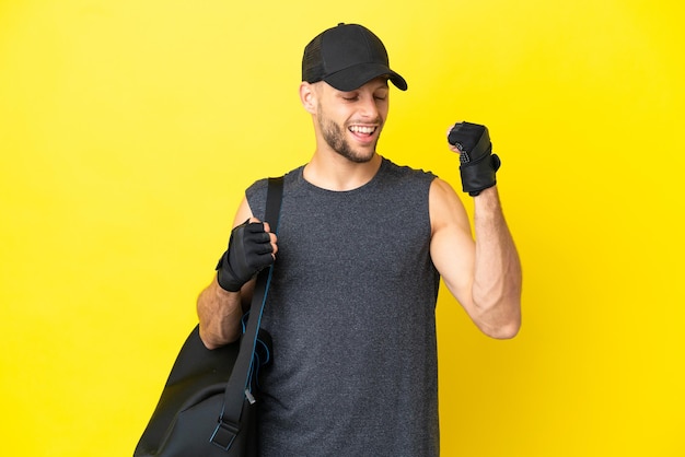 Foto joven deportista rubio con bolsa deportiva aislada de fondo amarillo celebrando una victoria