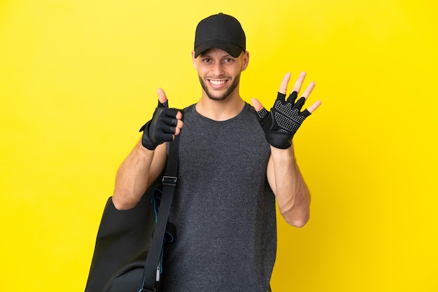 Joven deportista rubio con bolsa deportiva aislada de fondo amarillo contando seis con los dedos