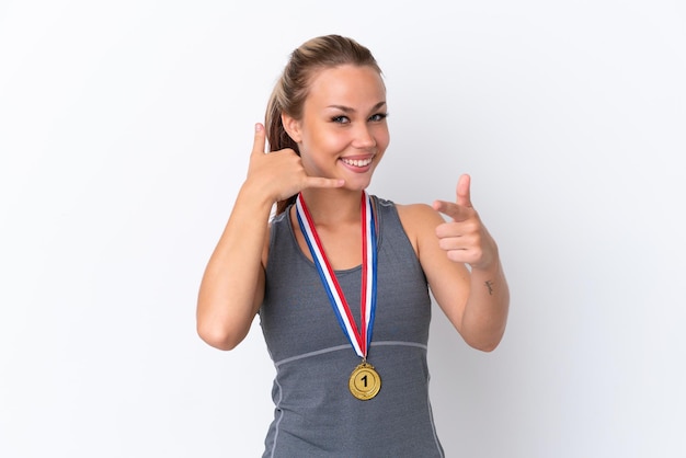 Joven deportista rusa con medallas aisladas de fondo blanco haciendo gestos telefónicos y apuntando al frente