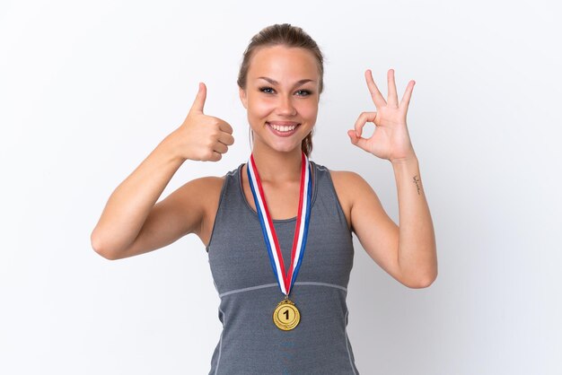 Joven deportista rusa con medallas aisladas en fondo blanco mostrando el signo de ok y gesto de pulgar hacia arriba