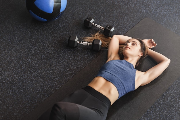 Joven deportista soñadora de ángulo superior acostado sobre una alfombra de goma en el piso del gimnasio.