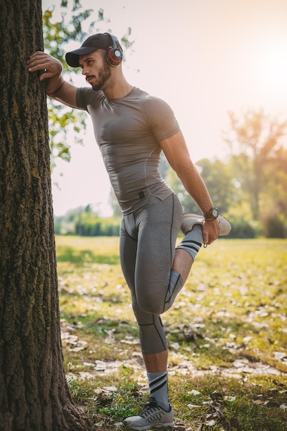 Joven deportista sonriente con auriculares haciendo ejercicio de estiramiento en la naturaleza.