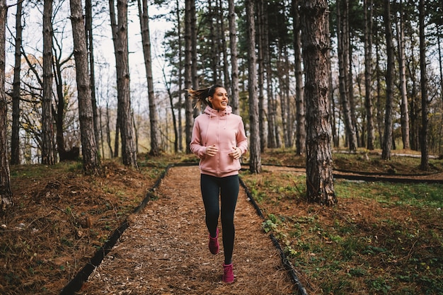 Joven deportista sonriente con hábitos saludables corriendo en el bosque en otoño y preparándose para el maratón.