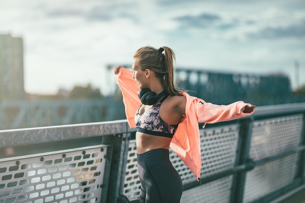 Una joven deportista viste una sudadera y se prepara para el entrenamiento matutino en un puente fluvial.