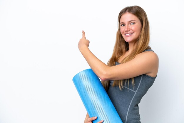 Joven deportista yendo a clases de yoga mientras sostiene una colchoneta apuntando hacia atrás