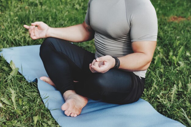 Joven deportista yogui sentado en posición de yoga de loto en el parque de césped al aire libre