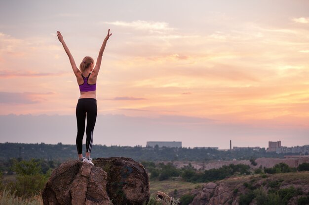 Foto joven deportiva con los brazos levantados al atardecer