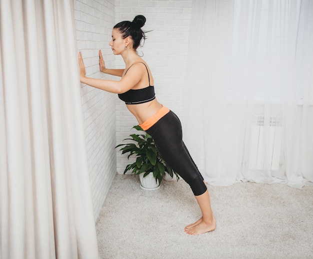 Una joven deportiva hace ejercicio en casa. chica delgada, practica deportes en una colchoneta de fitness en casa, se agacha con las manos.