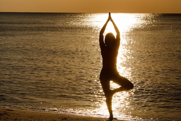 Joven deportiva haciendo ejercicios de yoga en la playa