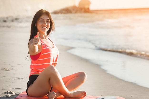 Joven deportiva haciendo ejercicios de yoga en la playa