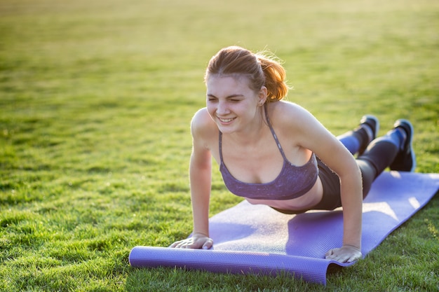 Joven deportiva en ropa deportiva entrenamiento en campo al amanecer.