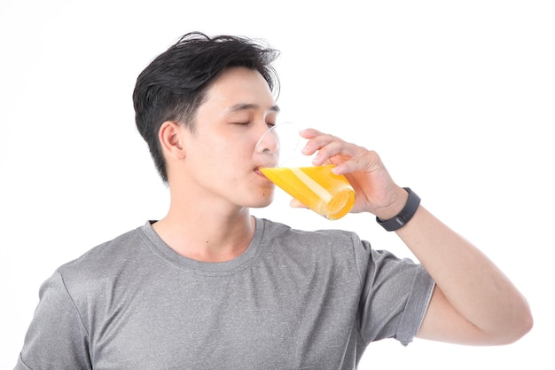 Joven deportivo asiático, apuesto y alegre, con un vaso de jugo de naranja con vitamina C aislado en el fondo