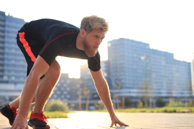 Joven deportivo en posición inicial al aire libre al atardecer o al amanecer