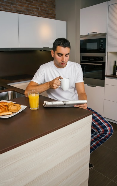 Joven desayunando en la cocina y leyendo el periódico