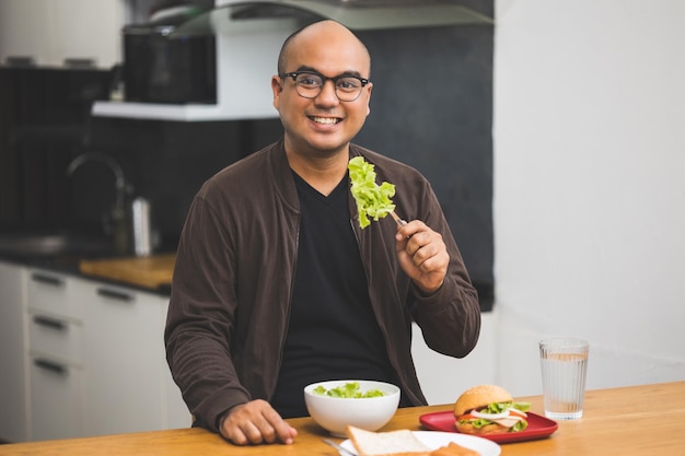 Un joven desayunando ensalada. Roble verde y tomates, los pinchó con un tenedor y comió y masticó deliciosamente.