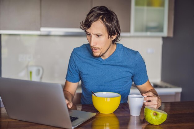 Joven desayunando y usando una laptop en la cocina