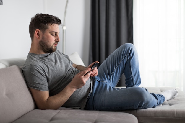 Joven descansando en el sofá con teléfono inteligente