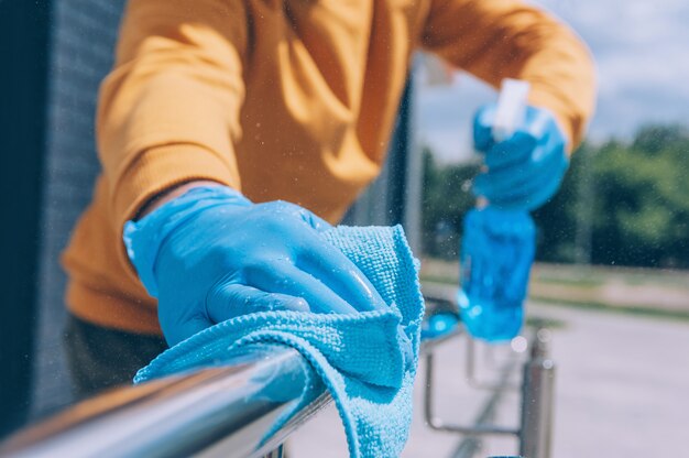 Joven desinfecta una barandilla con un antiséptico azul y un trapo en la mano