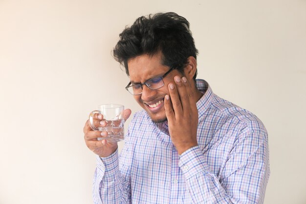 joven con dientes sensibles y vaso de agua fría.