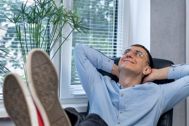 Joven director descansa en su oficina, poniendo los pies sobre la mesa. El gerente reflexiona sobre el trabajo.