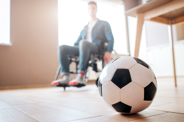 Joven con discapacidad sentado en silla de ruedas y mirar hacia abajo en la pelota para el juego. Ex deportista. Molesto e infeliz. Trauma. Ya no puedo jugar al fútbol.