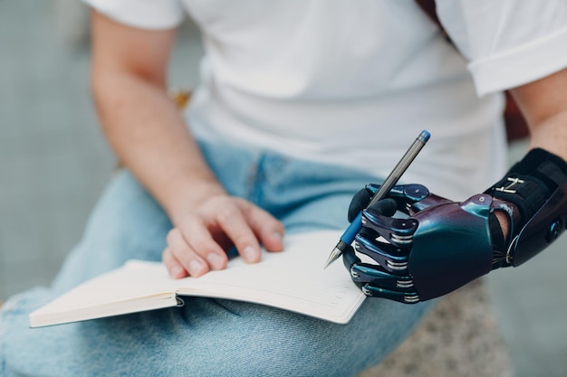 Joven discapacitado escribe en cuaderno con bolígrafo en mano protésica artificial