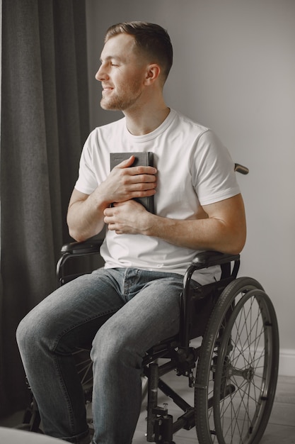 Joven discapacitado. Hombre leyendo un libro en silla de ruedas, quedarse en casa.