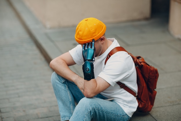 Joven discapacitado molesto a hombre triste con prótesis artificial sentado en la acera de la calle de la ciudad al aire libre