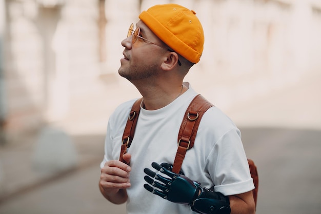 Joven discapacitado con prótesis artificial de mano en ropa casual y mochila caminando en la calle soleada de la ciudad al aire libre