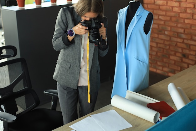 Joven diseñadora concentrada usando una cámara digital mientras está de pie cerca del escritorio en su oficina creativa.