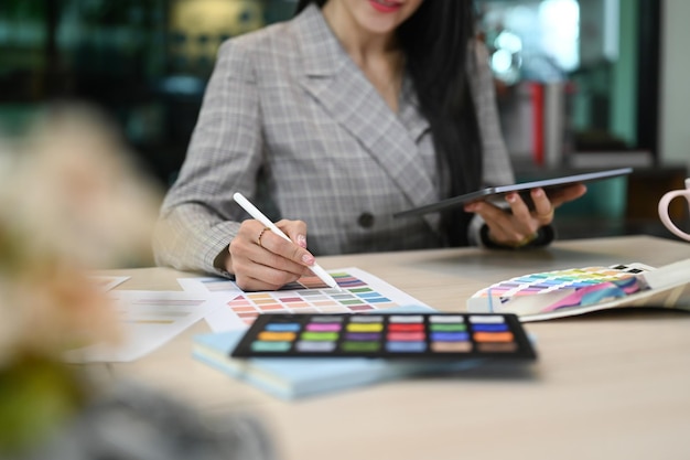 Joven diseñadora de interiores que trabaja con muestras de color y usa una tableta digital en su lugar de trabajo