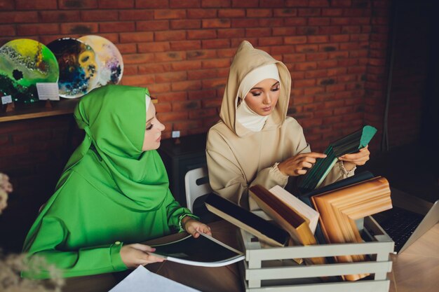 Joven diseñadora musulmana asiática que usa una tableta gráfica mientras trabaja con una computadora en el estudio o la oficina