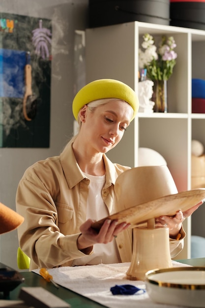 Joven diseñadora rubia de sombreros poniendo una pieza de madera en el tallo