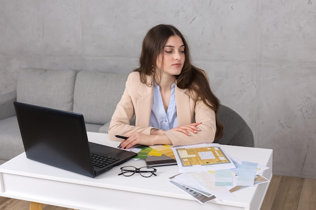 Una joven diseñadora sentada en una mesa dibuja en una tableta Hace cálculos comerciales en la computadora