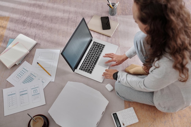 Joven diseñadora de ux sentada en el suelo en casa y trabajando en un proyecto