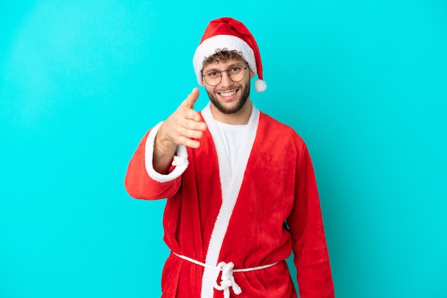 Joven disfrazado de Santa Claus aislado sobre fondo azul un apretón de manos para cerrar un buen trato