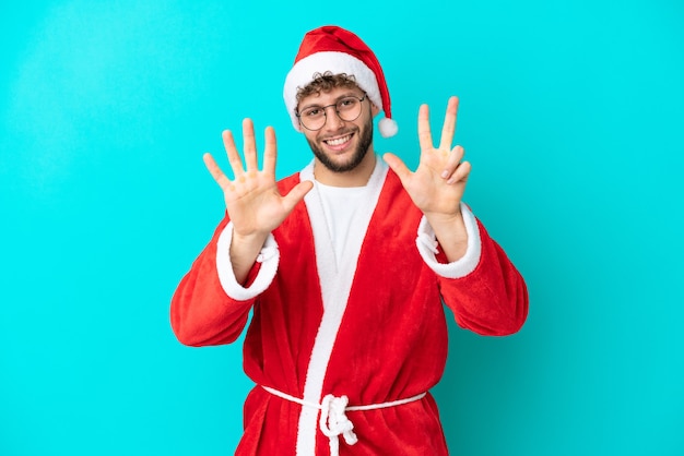 Joven disfrazado de Santa Claus aislado sobre fondo azul contando ocho con los dedos