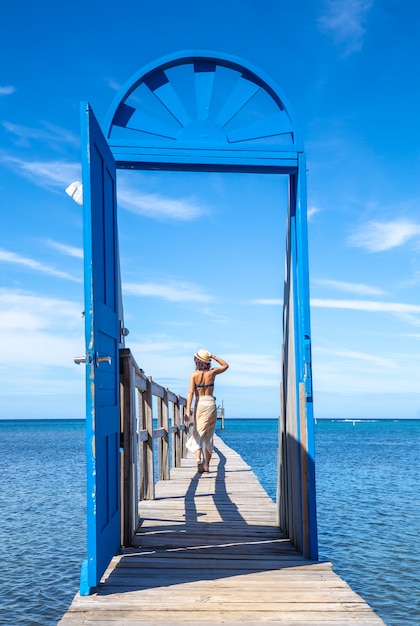 Una joven disfrutando detrás de la puerta azul en una pasarela de madera en la isla caribeña de Roatán en Honduras