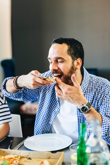 Joven disfrutando de una rebanada de pizza en la mesa de comedor