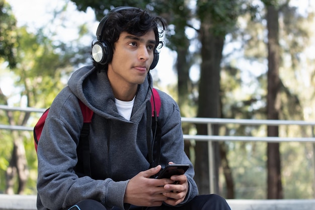 Joven disfrutando de un tiempo solo relajándose escuchando música con sus auriculares en el parque, tiene una sonrisa en la cara y una expresión facial de paz y bienestar.