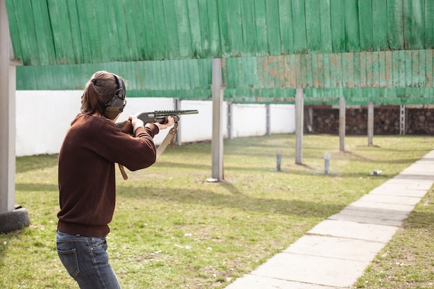 Foto un joven dispara a banderas metálicas, objetivos. escopeta de bombeo de armas de fuego.