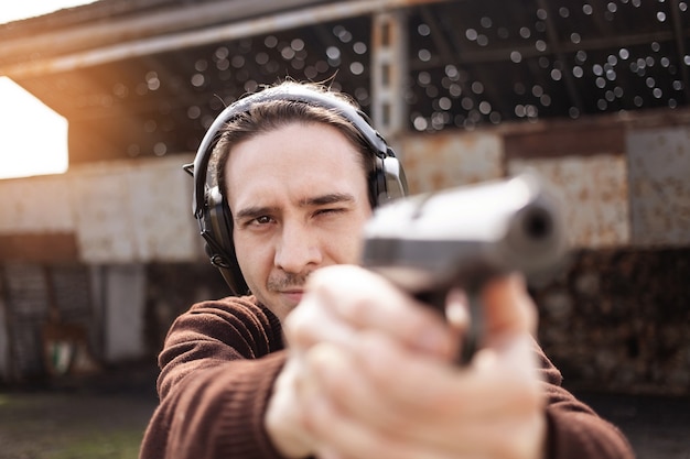 Un joven dispara una pistola, apuntando al objetivo. Un hombre con auriculares protectores.